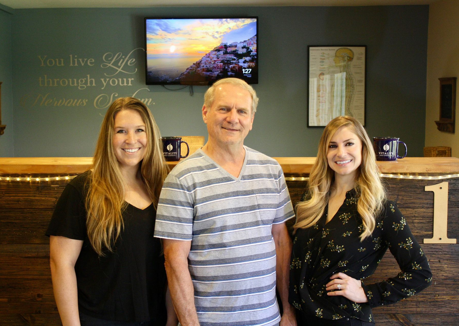 Three people standing together in front of a reception desk, smiling in a lobby.