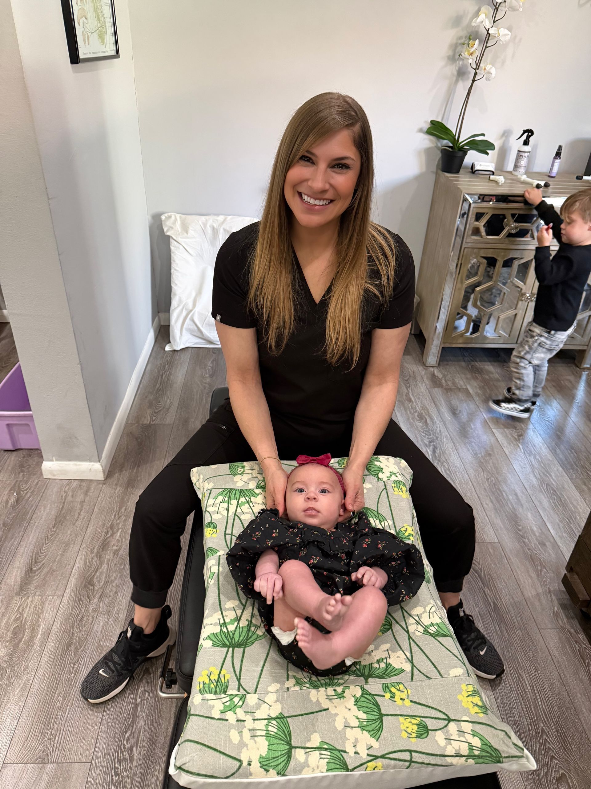 Woman smiling on the floor beside a baby lying on a green patterned mat in a bright room