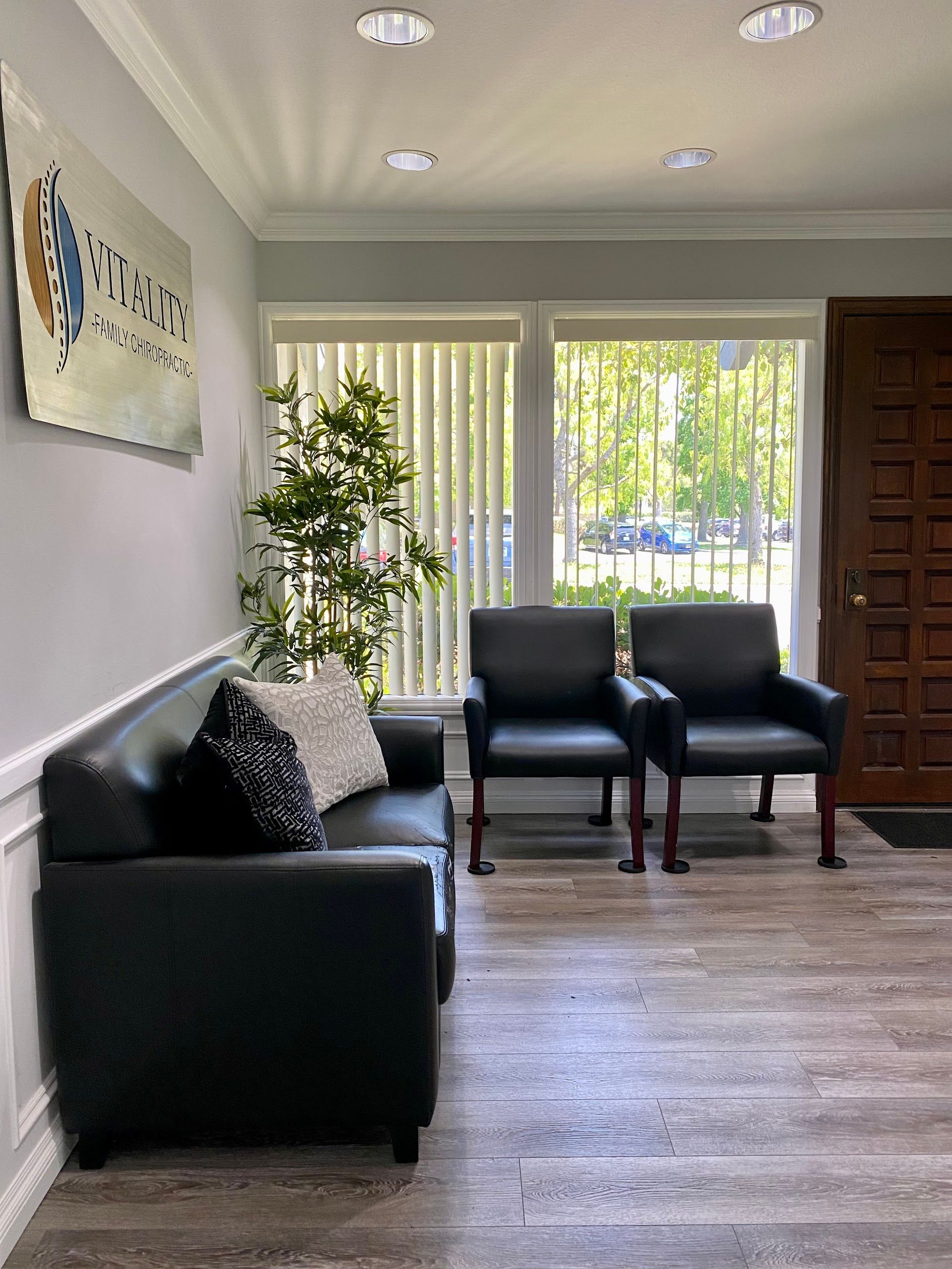 Modern waiting room with black chairs, plant, wall art, and sliding glass doors to a bright outdoor view