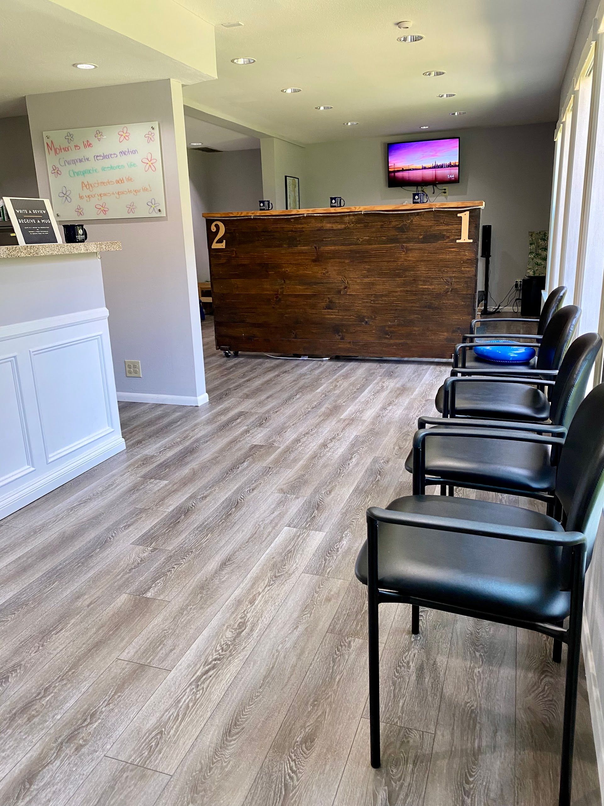 Bright waiting room with black chairs, wood reception desk, and TV on the wall