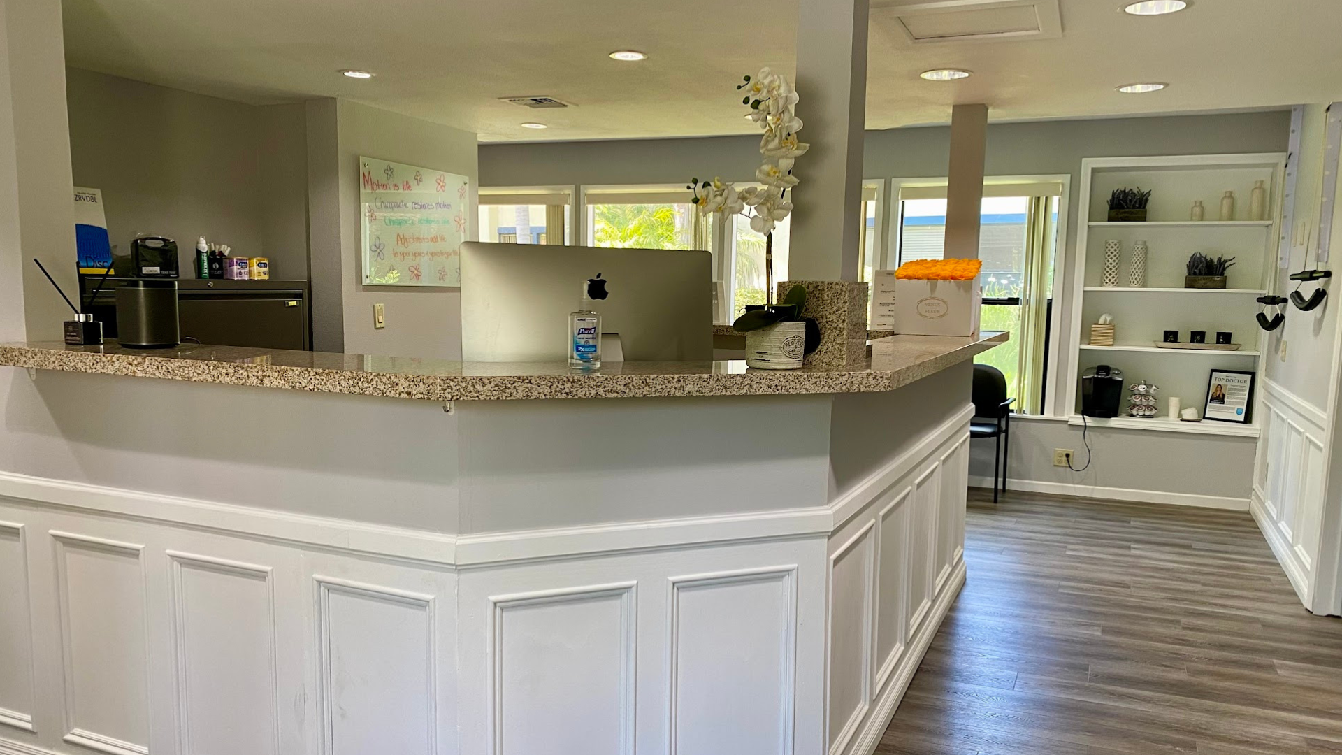 Empty reception counter in a bright, beige-and-white office lobby with wood floors and built-in shelves