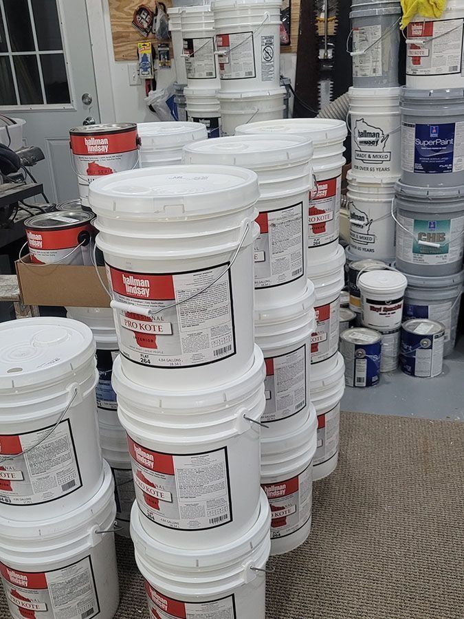 Stacks of white plastic paint buckets in a store aisle, with more containers on shelves behind them
