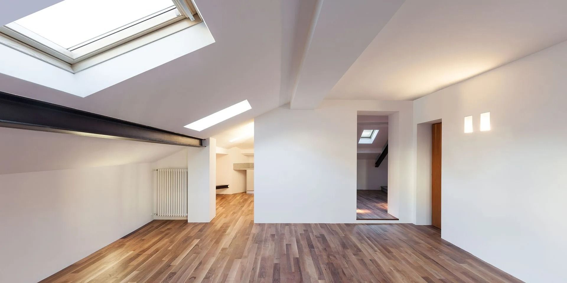 Empty modern loft room with skylight, wood floor, white walls, and open doorway