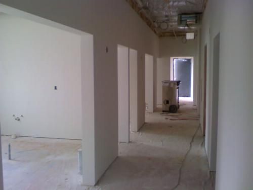 Empty unfinished hallway with white walls, exposed ceiling, and construction materials at the far end
