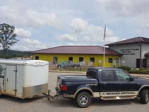 Pickup truck towing a white trailer outside a yellow public building under a cloudy sky