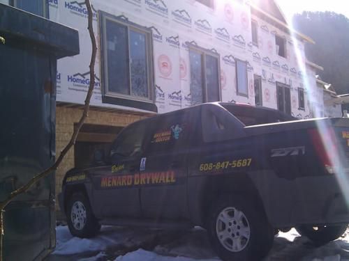 Black SUV parked outside a building under construction with sun glare and pink insulation visible