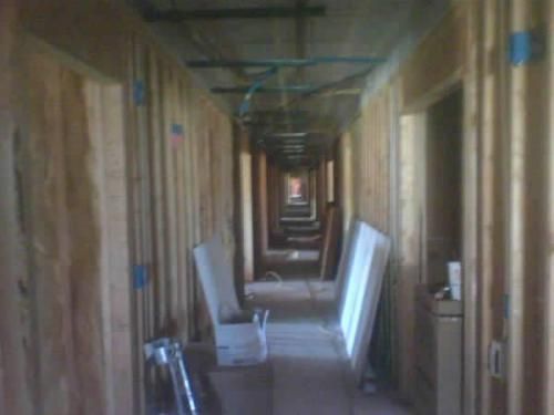Long, narrow hallway with wooden walls and doors, lined with chairs and leaning boards.