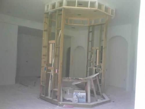 Partially built wooden frame structure inside an unfinished room with tools and materials on the floor