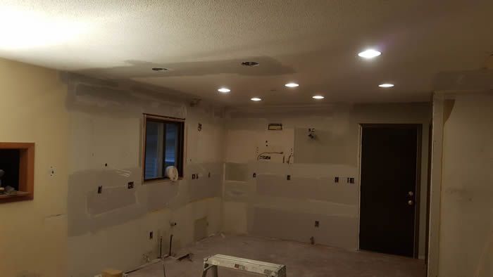 Empty kitchen under renovation with recessed ceiling lights, unfinished walls, and a dark doorway.