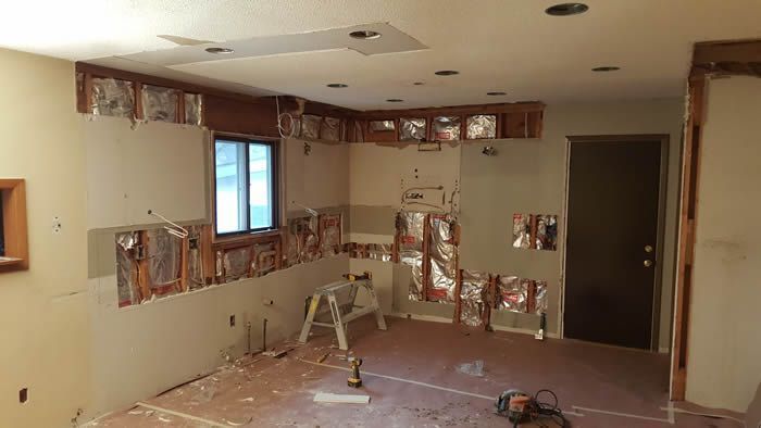 Partially demolished room with exposed wall studs, debris, and a ladder during renovation