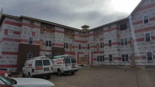 Partially completed multi-story building with red-and-white facade and two white vans parked outside
