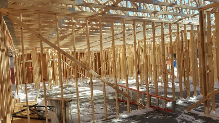Wood-framed house under construction with exposed studs, floor joists, and sunlight streaming through the structure
