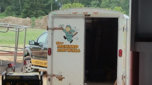 White U-Haul truck with rear door open, showing a cartoon logo on the side, parked near other vehicles outdoors