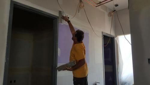 Person reaching up to work on ceiling wiring in a room with open doorways