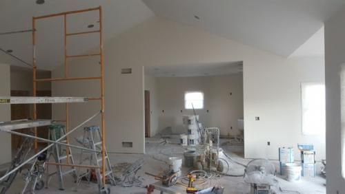 Renovation site with scaffolding, tools, and debris in an unfinished white room with a large opening