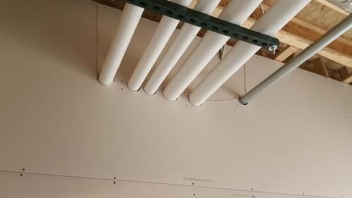 White pipes and a metal track mounted near a ceiling above a beige wall