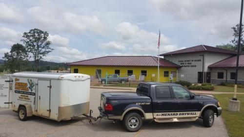 Black pickup truck towing a white trailer in front of a yellow building under cloudy skies