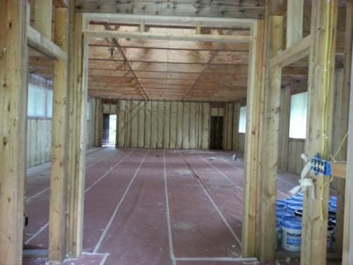 Interior of a framed house under construction with exposed wood walls, beams, and unfinished subfloor.