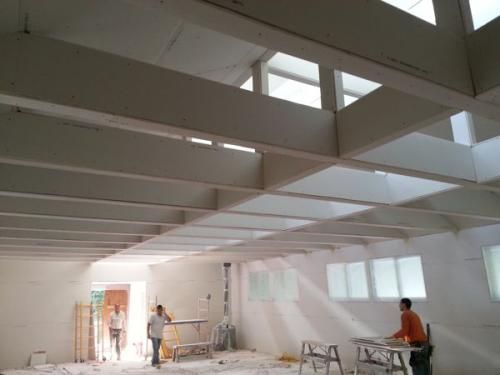 White loft-like room under construction with exposed beams and workers painting and setting up ladders