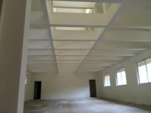 Empty white industrial room with high ceiling beams, windows, and two dark doorways.