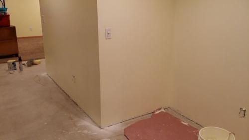 Partially finished room with beige walls, bare floor, and renovation materials in the corner