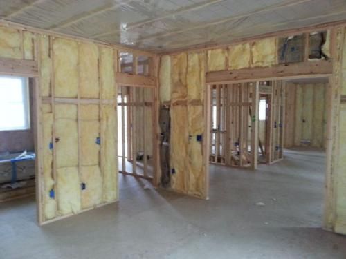 Framed interior under construction with exposed yellow insulation and unfinished walls