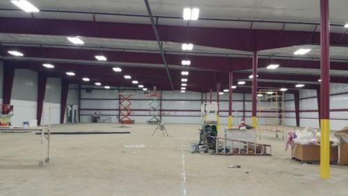Empty warehouse interior with metal beams, scaffold, and equipment under bright overhead lights