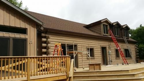 Workers on ladders repainting a log-style house exterior with a wooden deck in front