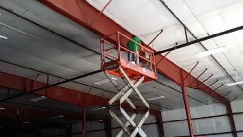 Worker in a red scissor lift inspecting the ceiling inside a warehouse.