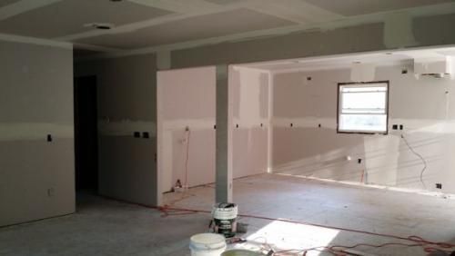 Unfinished room under renovation with exposed drywall, paint buckets, and construction materials on the floor.