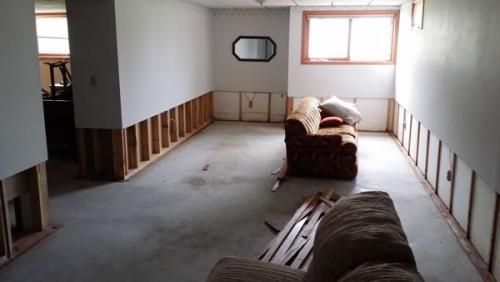 Unfinished room with exposed wall studs, a couch, bench, and a window letting in daylight.