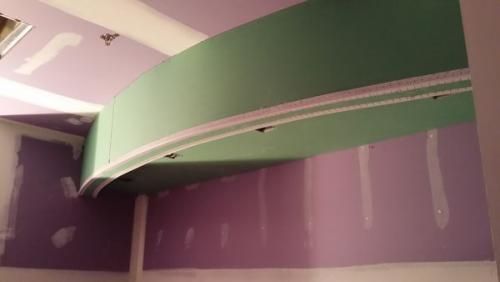 Curved green ceiling feature in a purple room with white trim and exposed drywall patches