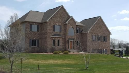 Large brick suburban house with a green lawn and leafless trees under a cloudy sky