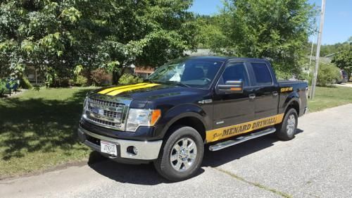 Black pickup truck with yellow lettering parked on a sunny suburban street.