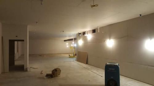 Empty unfinished room with bare concrete floor, beige walls, and construction materials near the wall.