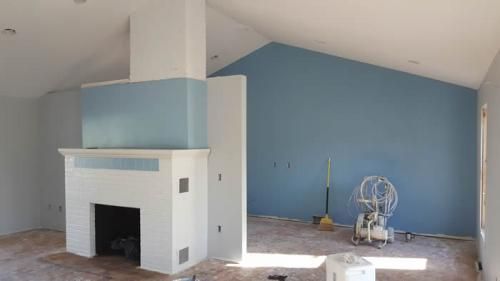 Living room with blue accent wall, white fireplace, and construction materials on the floor