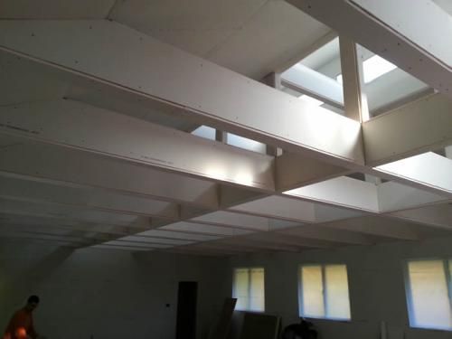 Empty room with white ceiling beams and skylights, and small windows along the wall.
