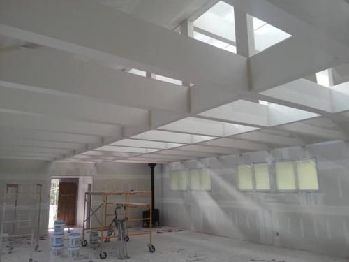 Empty white room under renovation with exposed beams, skylights, and construction supplies on the floor