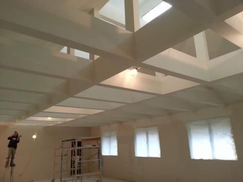 Interior with white ceiling beams, recessed lights, windows, and workers on scaffolding during renovation