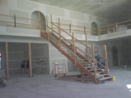 Scaffolded staircase in an unfinished building interior with exposed walls and dust-covered floors