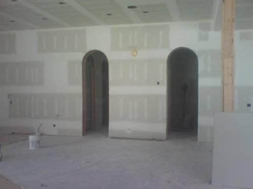 Empty unfinished room with drywall, arched doorways, and bare concrete floor