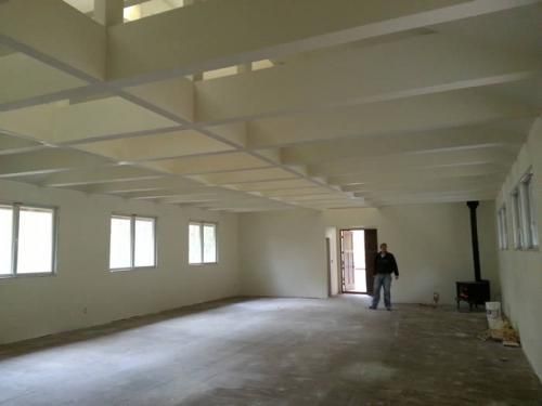 Empty unfinished room with white walls, exposed ceiling beams, and a person standing near the far doorway.