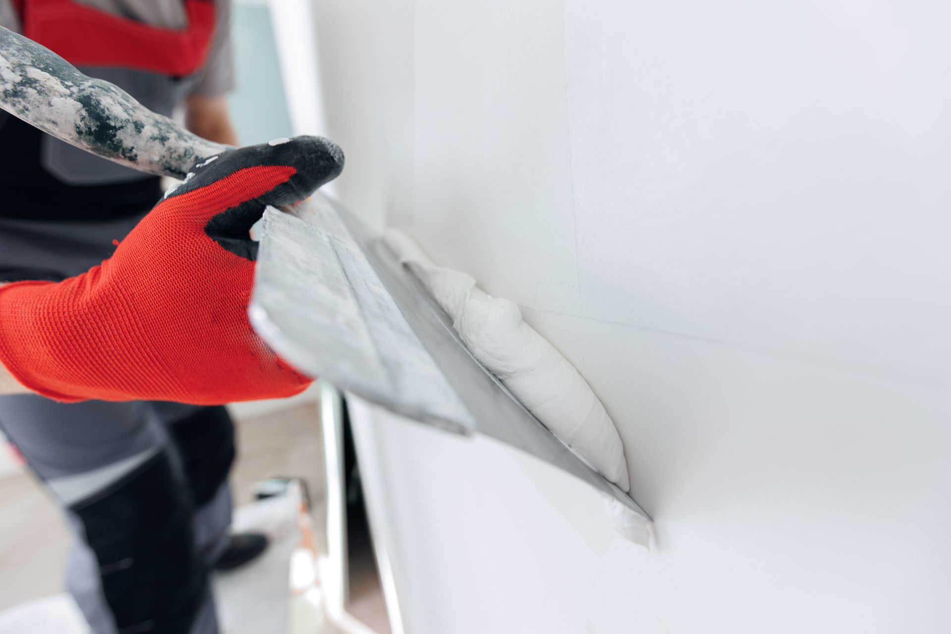 Red-gloved hand applying joint compound to a white wall seam with a putty knife
