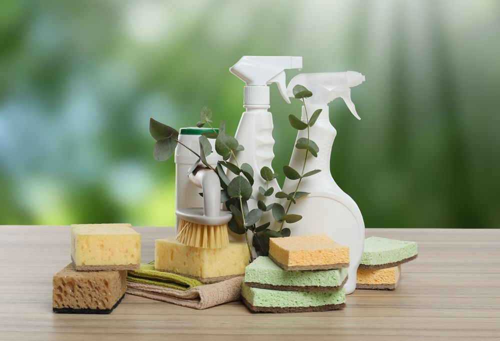 Cleaning supplies and sponges arranged on a wooden surface with a blurred green background