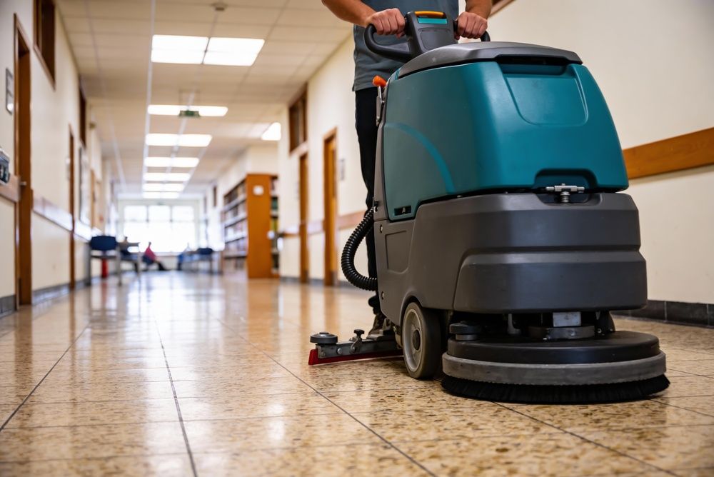 Floor cleaning machine being operated in a long, empty hallway with tiled floor.