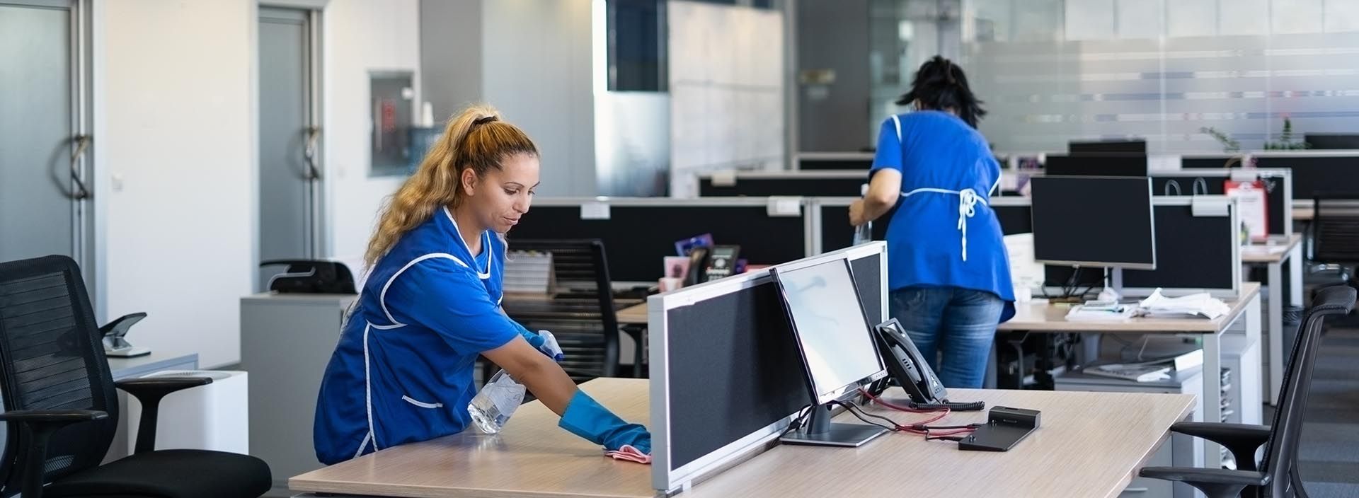 Office workers in blue uniforms cleaning and organizing computers in a modern workspace