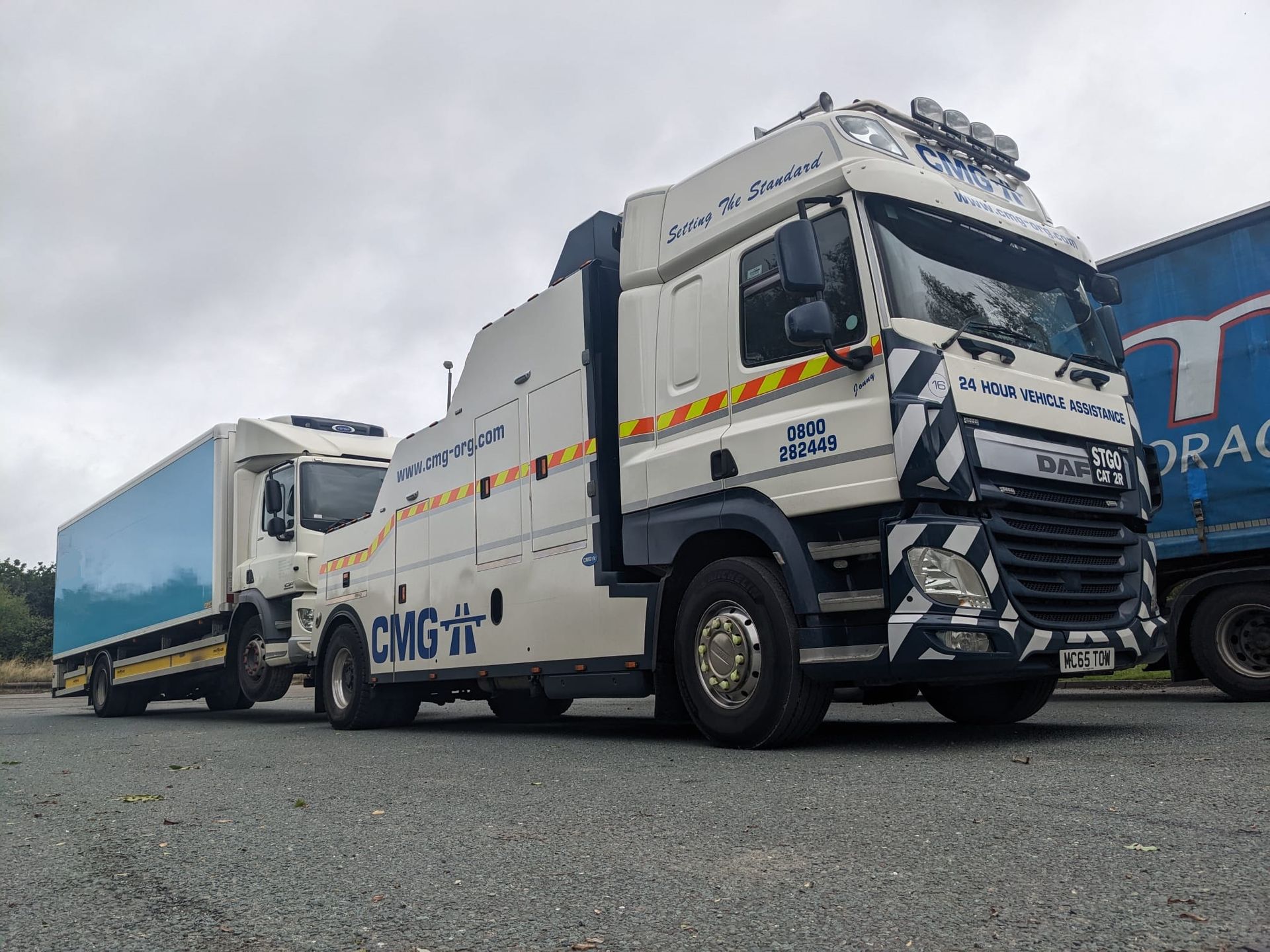Two white tow trucks parked side by side on a gravel lot under a cloudy sky