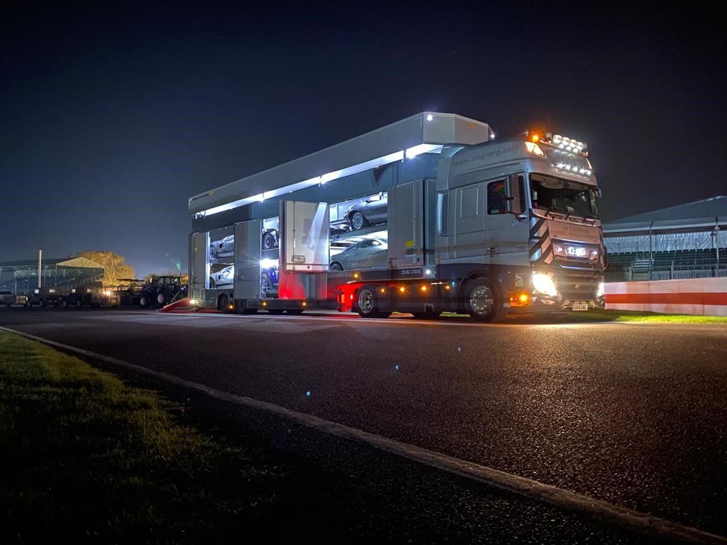 a multi-car transporter carrying classic cars pared on a race track
