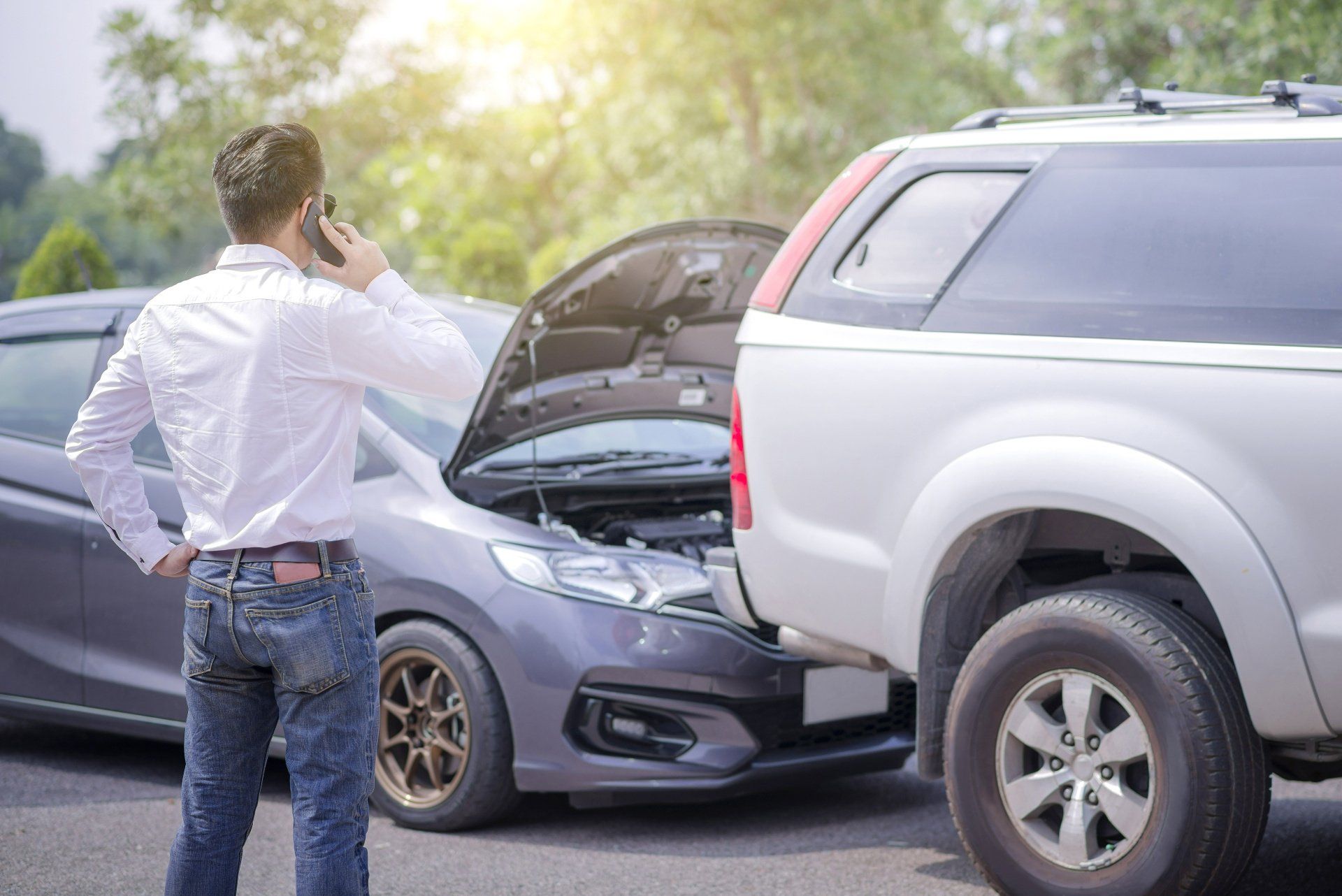 A man is talking on a cell phone in front of a car accident.