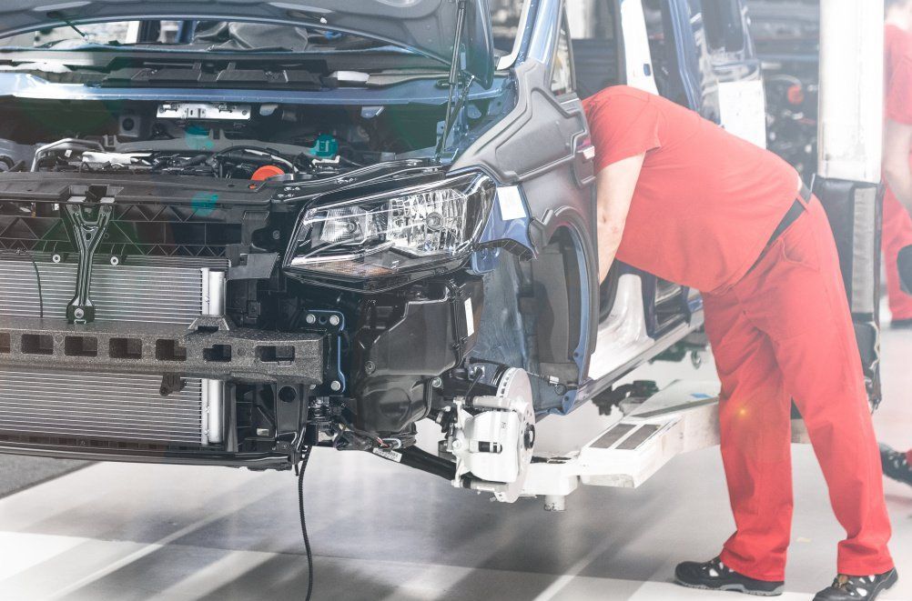 A man in red pants is working on a car in a factory.